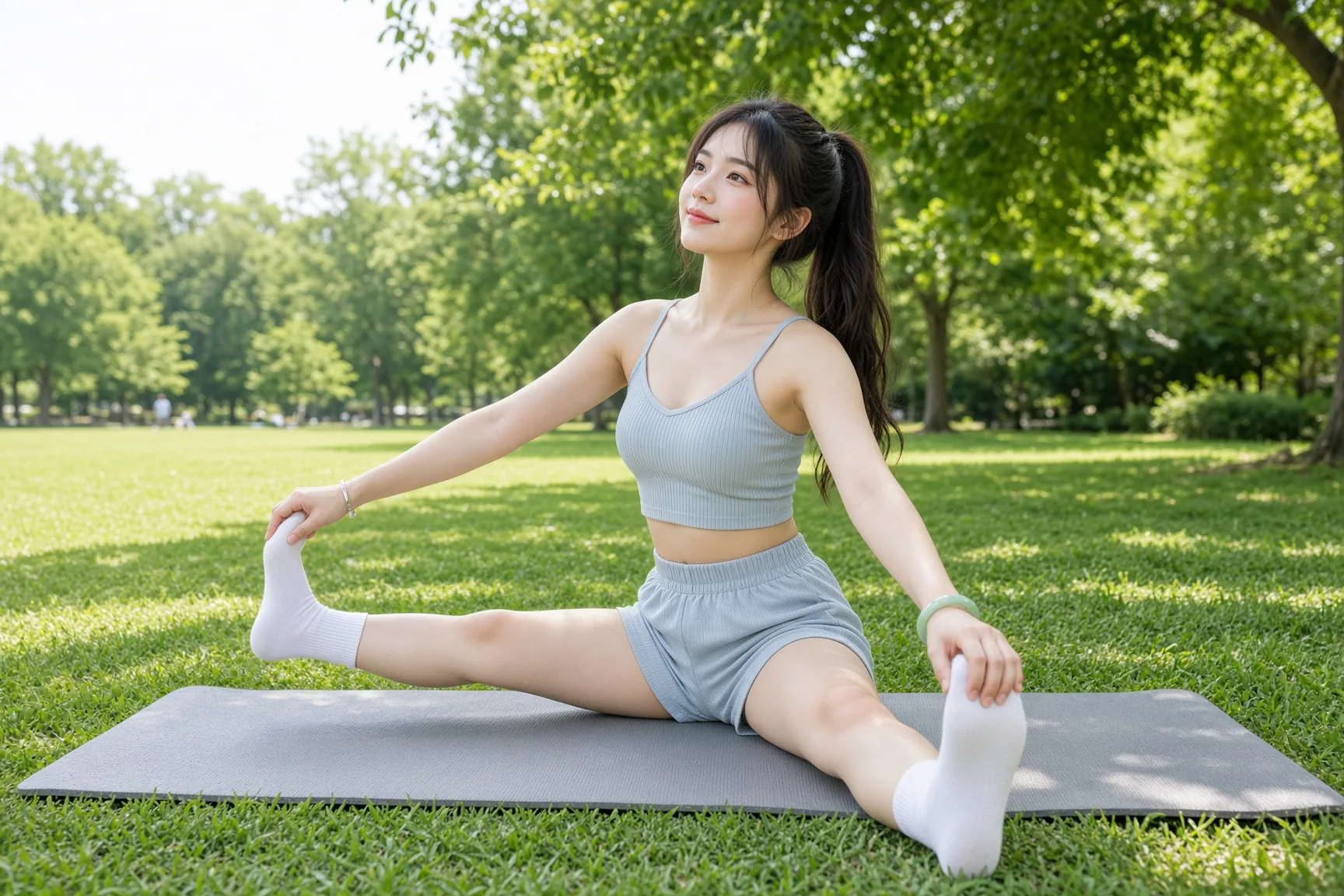 Young woman in a gray athletic outfit stretching on a yoga mat in a sunny green park